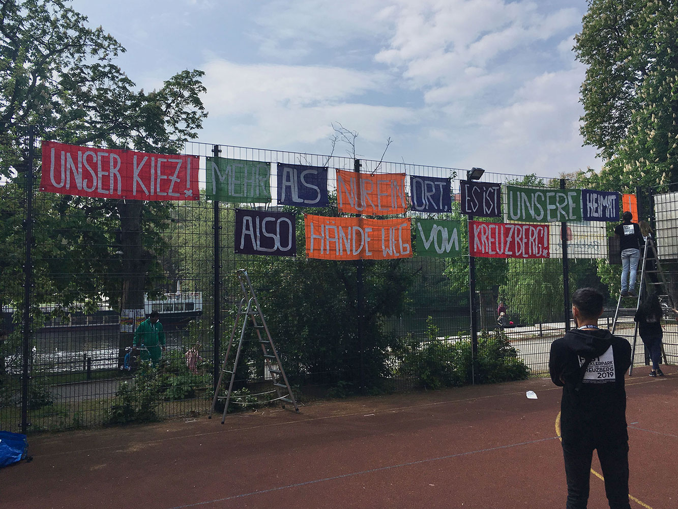 Abb. 4 Jugendliche befestigen für das MaiFest (2019) ein selbstgemaltes Banner am Zaun eines Kreuzberger Kinder- und Jugendzentrums (Quelle: eigene Aufnahme)